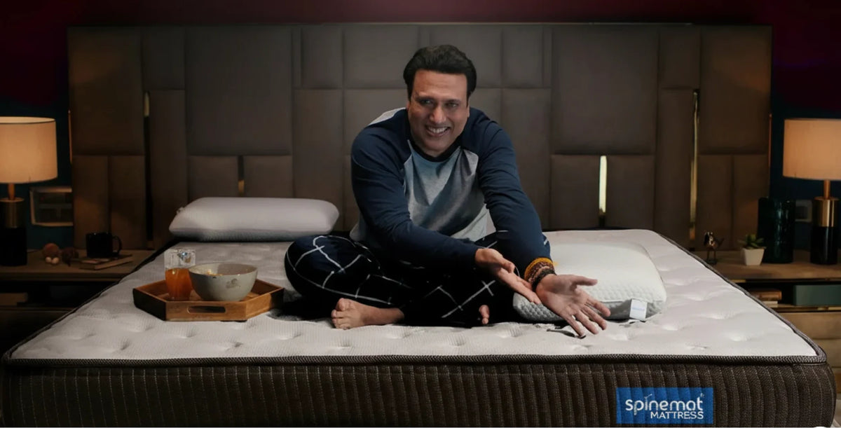 SpineMat brand ambassador Govinda seated on a SpineMat mattress in a warmly lit bedroom